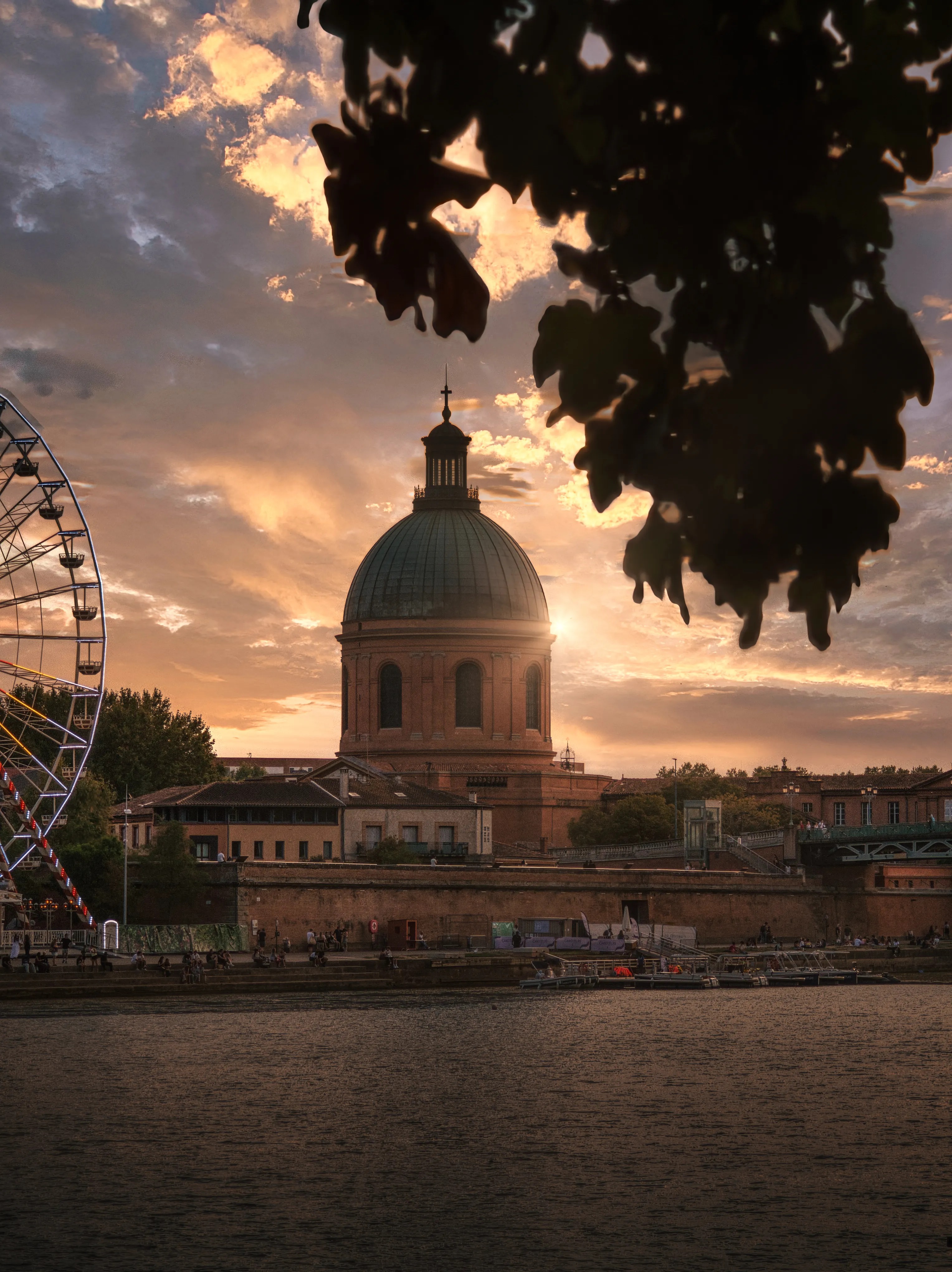 A domed building across the Garonne at sunset, framed by leaves